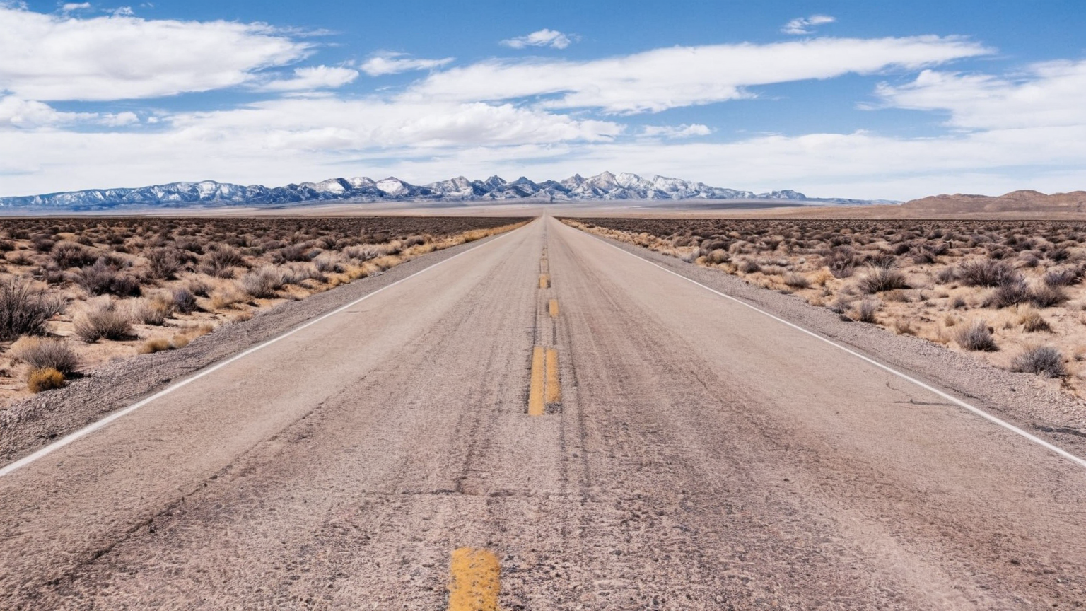 West Texas two-lane desert highway with dashed yellow center line stretching toward distant mesas under a bright daytime sky